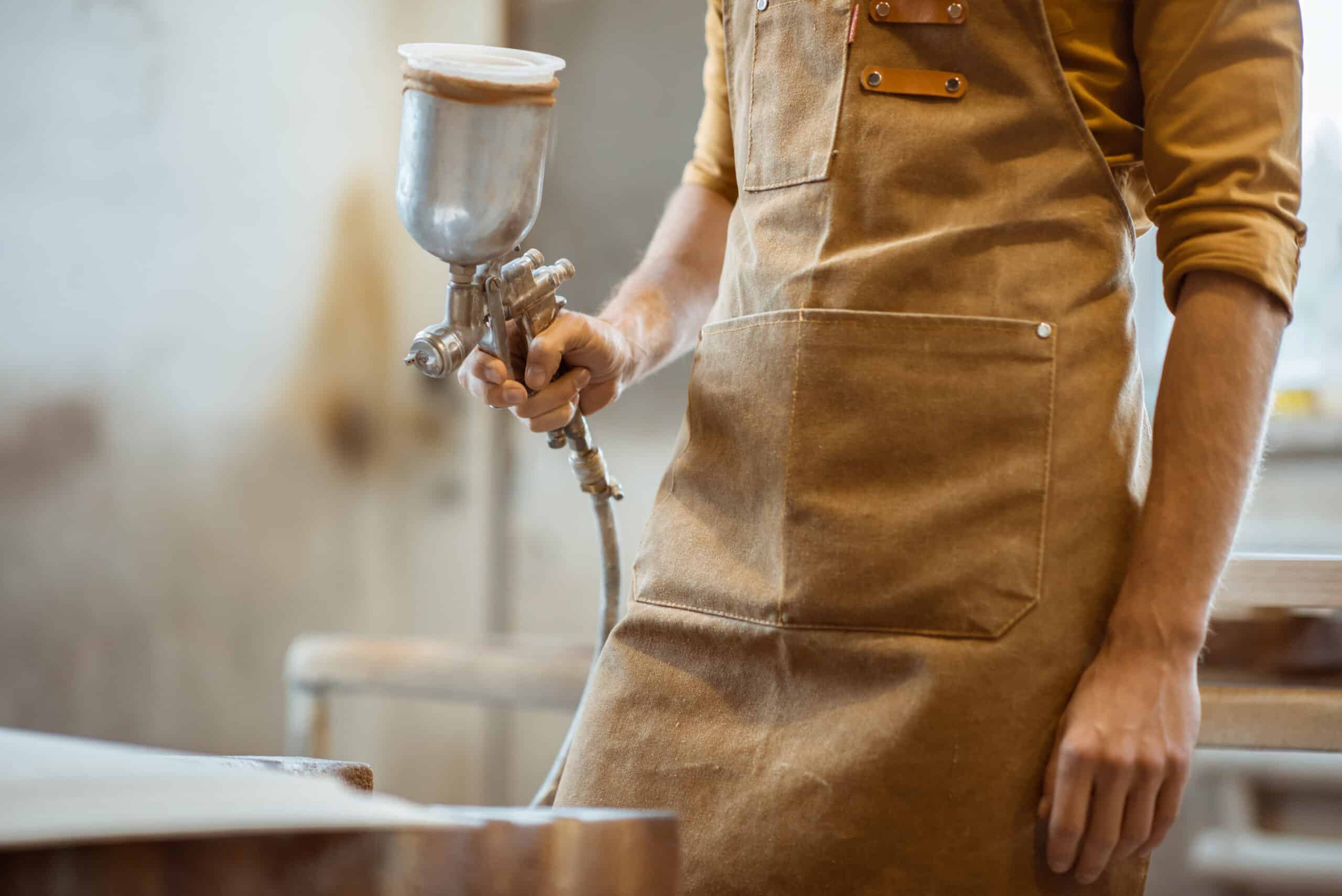 Painting wooden product with a spray gun at the painting shop of the carpentry, close-up