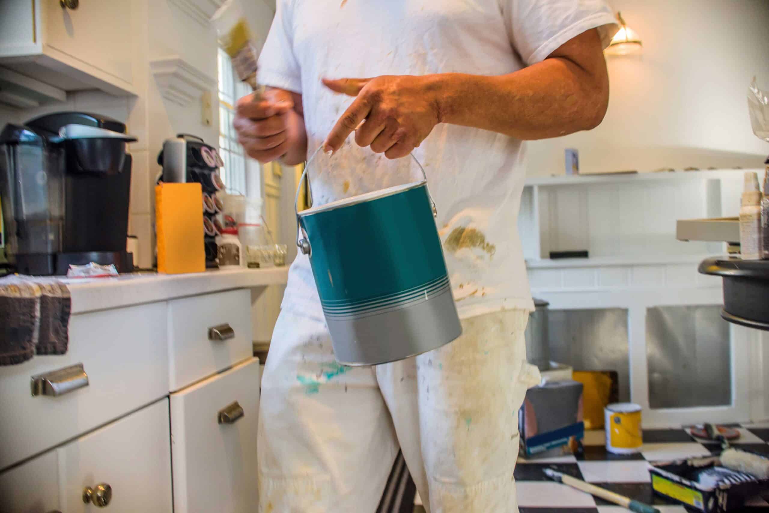 man in kitchen holding primer paint for cabinet